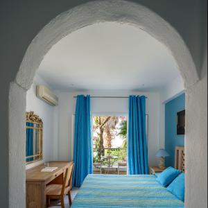 1 dormitorio con cortinas azules, 1 cama y escritorio en Alesahne Beach Hotel, en Kamari