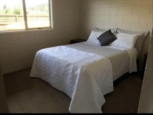 Un dormitorio con una cama blanca con una ventana. en Waetford Road Lodge, en Matapouri