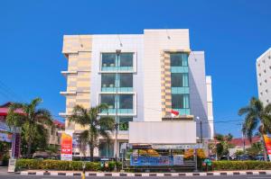 a tall white building with palm trees in front of it at Daima Hotel Padang in Padang