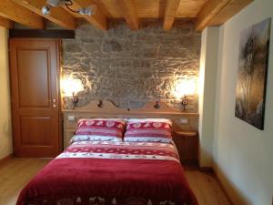 una camera da letto con un letto con lenzuola rosse e un muro in pietra di Alpe di Sara a Fiumalbo