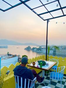 a man sitting at a table on a balcony overlooking the water at Hostel Mantra in Udaipur