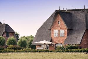 a house with a thatched roof with an umbrella at SalzWasserHerz Senhoog Luxury Holiday Homes ***** in Morsum