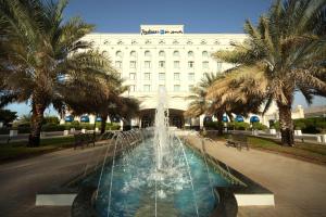 uma fonte em frente a um edifício com palmeiras em Radisson Blu Hotel, Muscat em Mascate