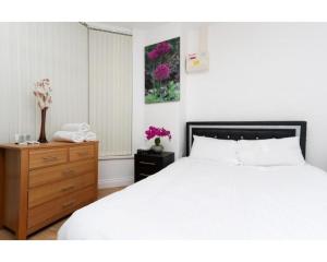 a bedroom with a white bed and a wooden dresser at Balmain Apartments in Leeds
