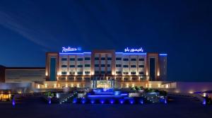 Radisson Blu Hotel & Resort, Sohar في صحار: فندق فيه اضاءه زرقاء امام مبنى