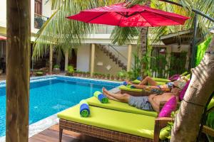 two people laying in lawn chairs next to a swimming pool at Rosy Villa Hotel in Guraidhoo