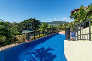 a blue swimming pool with a fence and trees at Ambience of Airlie - Airlie Beach in Airlie Beach