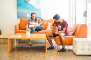 Um homem e uma mulher sentados num sofá a tocar guitarra. em The Island Accommodation em Phillip Island