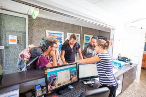 eine Gruppe von Personen, die um einen Schreibtisch mit einem Computer stehen in der Unterkunft The Island Accommodation in Phillip Island