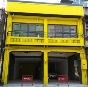un bâtiment jaune avec deux chaises rouges devant lui dans l'établissement 客旅家青年旅館 Travelers Plus, à Chiayi