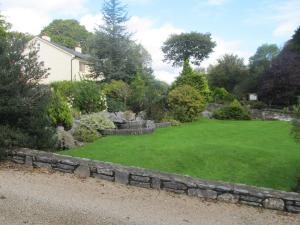 un jardín con una pared de piedra y césped verde en Neidin House en Kenmare