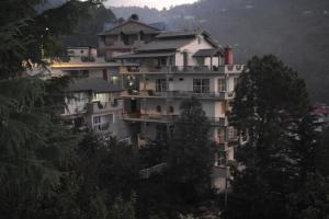 a large white building on a hill with trees at Clarks Exotica Resort Ramgarh Mukteshwar in Rāmgarh