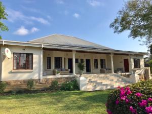 a white house with a porch and flowers at Bishops GuestHouse in Eshowe