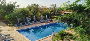 a large swimming pool with lounge chairs and trees at La Taniere Villa Metsu in Saly Portudal