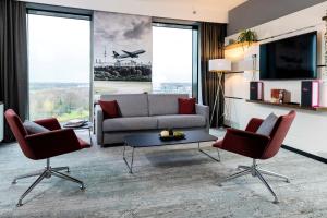 a living room with a couch and chairs and a tv at Airport Plaza Hotel Hamburg, vorher bekannt als Nordport Plaza Hotel in Norderstedt