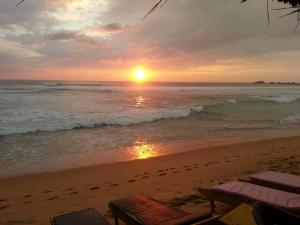 un tramonto sulla spiaggia con sedie e l'oceano di Main Reef Guest House a Hikkaduwa