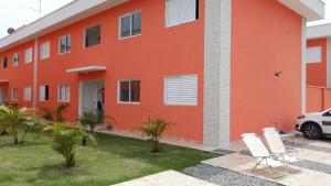 um edifício laranja com cadeiras brancas em frente em Apartamento Boracéia Bertioga em Bertioga