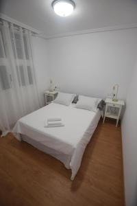 een witte slaapkamer met een groot wit bed en 2 tafels bij El Médano, apartamento céntrico y cerca del mar in Granadilla de Abona