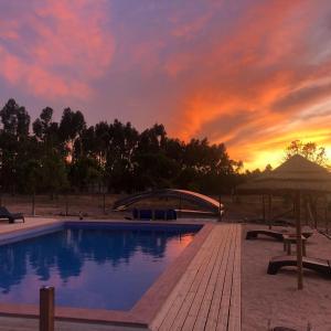 a swimming pool with a sunset in the background at Quinta das Beldroegas - Casas de Campo in São Teotónio