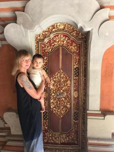 a woman holding a baby in front of a door at Kampung Sari Homestay in Ubud