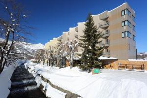 a building in the snow next to a river at Hotel Hakuba in Hakuba