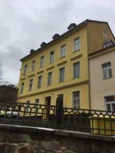 un bâtiment jaune avec une clôture devant lui dans l'établissement Margo Apartman, à Karlovy Vary