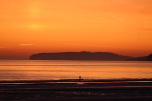 a person walking on the beach at sunset at Bungalow33 Benllech in Benllech