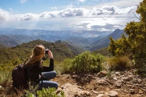 a woman sitting on a hill taking a picture of the mountains at La Posada del Angel in Ojén