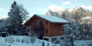 a house covered in snow with mountains in the background at Chalet les Vagnys - Lac des Vernays in La Rivière-Enverse