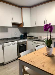 una cucina con armadi bianchi e un tavolo in legno con fiori viola di Lemos Nube a Monforte de Lemos