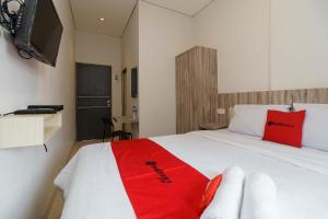 um quarto com uma cama branca e um cobertor vermelho em RedDoorz Syariah near RSUD Siti Fatimah Palembang em Palimbão