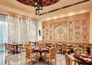 Taj Hotel & Convention Centre, Agra في آغْرا: غرفة طعام بها طاولات وكراسي وجدار
