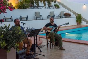 two men sitting in chairs playing guitar next to a pool at Castri Village Hotel in Palekastron