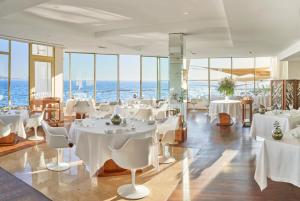 um restaurante com mesas e cadeiras brancas e o oceano em Le Petit Nice - Passedat em Marselha