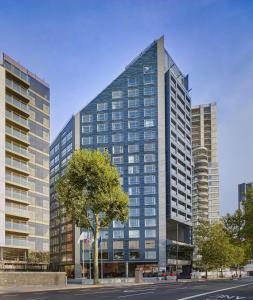 um edifício de vidro alto com uma árvore em frente em Park Plaza London Riverbank em Londres