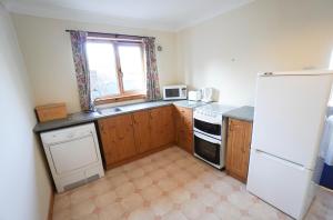 uma cozinha com armários de madeira e um frigorífico branco em Hamish's Cottage em Tobermory