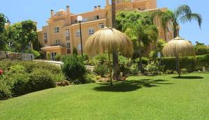 a large building with two straw umbrellas in a yard at Princess Park in Sitio de Calahonda