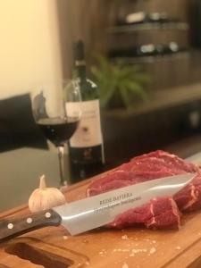 a knife on a cutting board with meat and a bottle of wine at Apartamento Vêneto in Canela