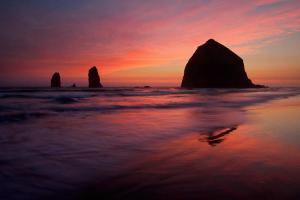 una puesta de sol en la playa con dos grandes rocas en el agua en Lighthouse Inn, en Cannon Beach