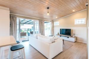 uma sala de estar com um sofá branco e uma televisão em Pohutukawa Cottage, Waiheke Island em Oneroa