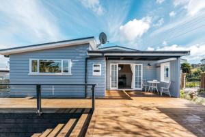 une maison bleue avec une terrasse et une table dans l'établissement Pohutukawa Cottage, Waiheke Island, à Oneroa