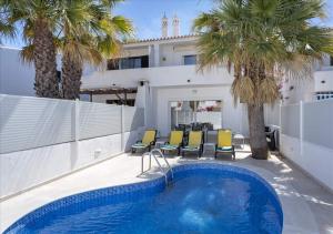 a swimming pool in front of a house with palm trees at Vicky Rae Beach House - Vale do Lobo in Almancil