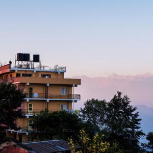 a building with trees and mountains in the background at Hotel Green Valley Nagarkot in Nagarkot