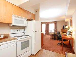 een keuken met witte apparatuur en een woonkamer bij Stonebridge Hotel Dawson Creek in Dawson Creek