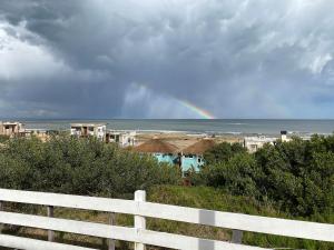 a rainbow over a beach with a white fence at Cabañas Punta Papaya in Punta Del Diablo