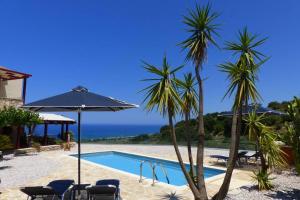 a pool with palm trees and chairs and an umbrella at Villa Miramare in Georgioupolis