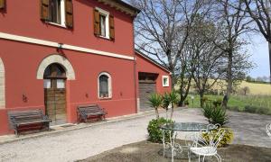 a red building with benches and a table in front of it at Casa Vacanze La Meridiana in Serrungarina