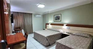 a hotel room with two beds and a desk at Brumado Hotel in Campo Grande