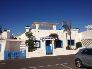 a white house with blue doors and a car parked in a parking lot at Mi casa su casa in La Oliva