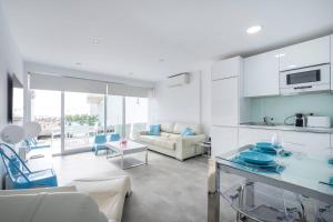 a kitchen and living room with white cabinets and blue chairs at Ciudad Blanca Apartment in Port d'Alcudia